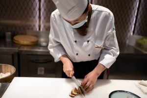 mulher cortando alimento em uma bancada de uma cozinha industrial