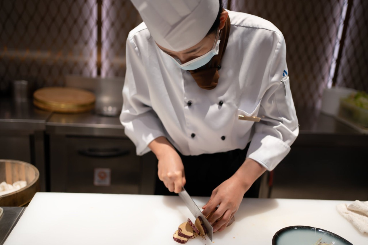 mulher cortando alimento em uma bancada de uma cozinha industrial